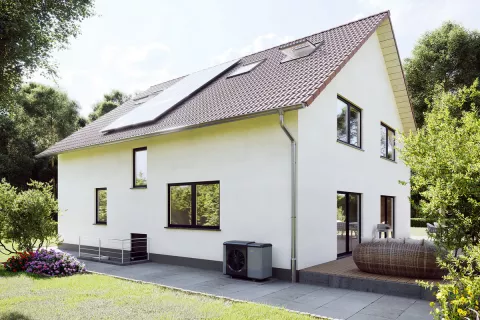 Eine perfekt passende Wärmepumpenheizung vor einem sanierten Einfamilienhaus im Außenbereich platziert.